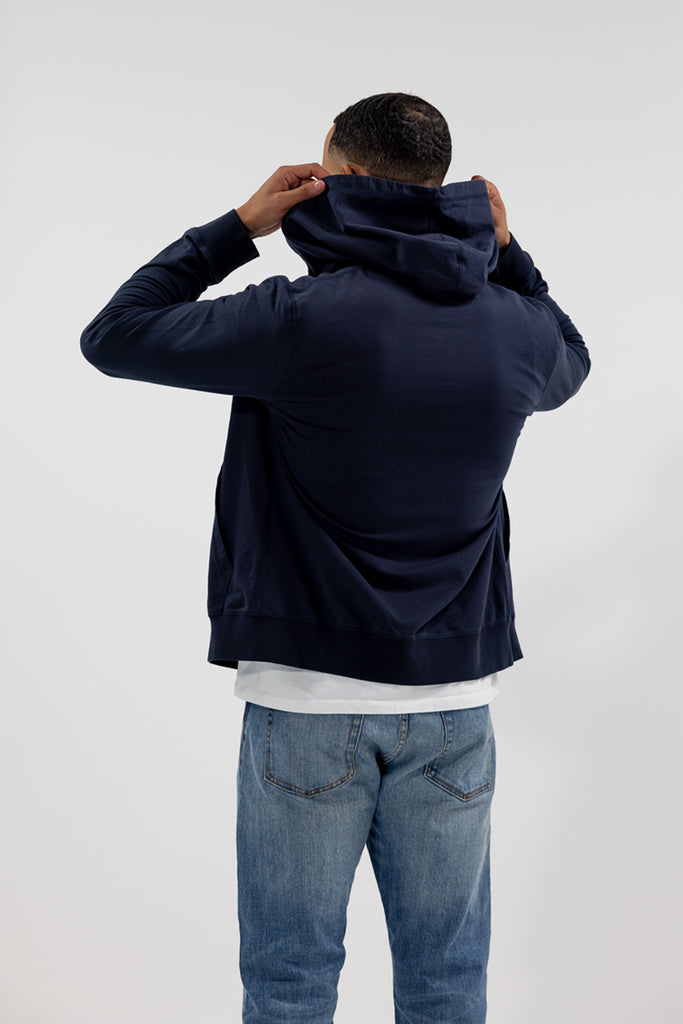 back view of model wearing Easy Mondays dark blue navy hoodie jacket putting on hood