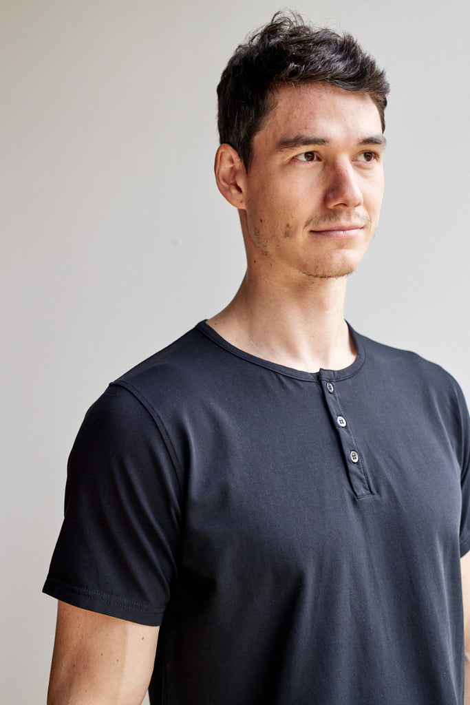 angled close up view of model wearing Easy Mondays black short sleeved Henley shirt with color-matched buttons
