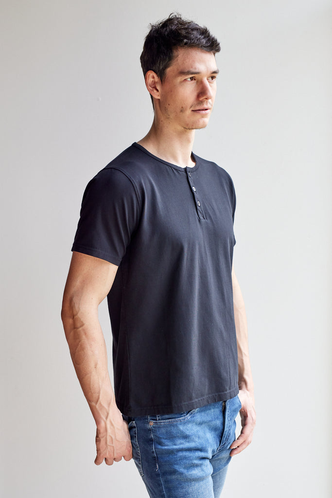 angled side view of model wearing Easy Mondays black short sleeved Henley shirt with color-matched buttons