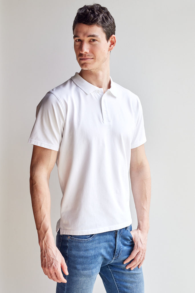 angled front view of model wearing Easy Mondays off white colored polo shirt with color-matched buttons looking into the camera with one thumb in pocket