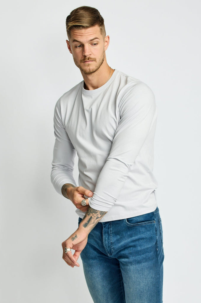 partial front view of model wearing Easy Monday long sleeve crew neck sweater in off-white cloud color tucking sleeve of crossed-over arm