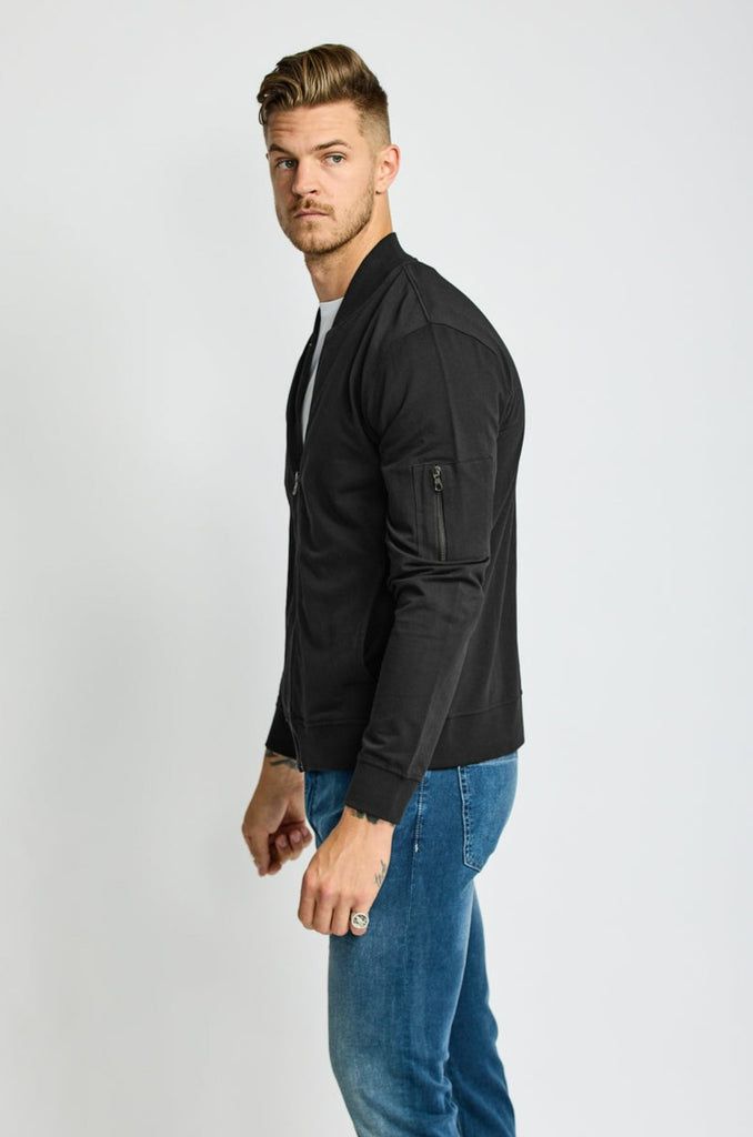 side of model wearing Easy Mondays brand full-zip black fleece bomber jacket halfway zipped up