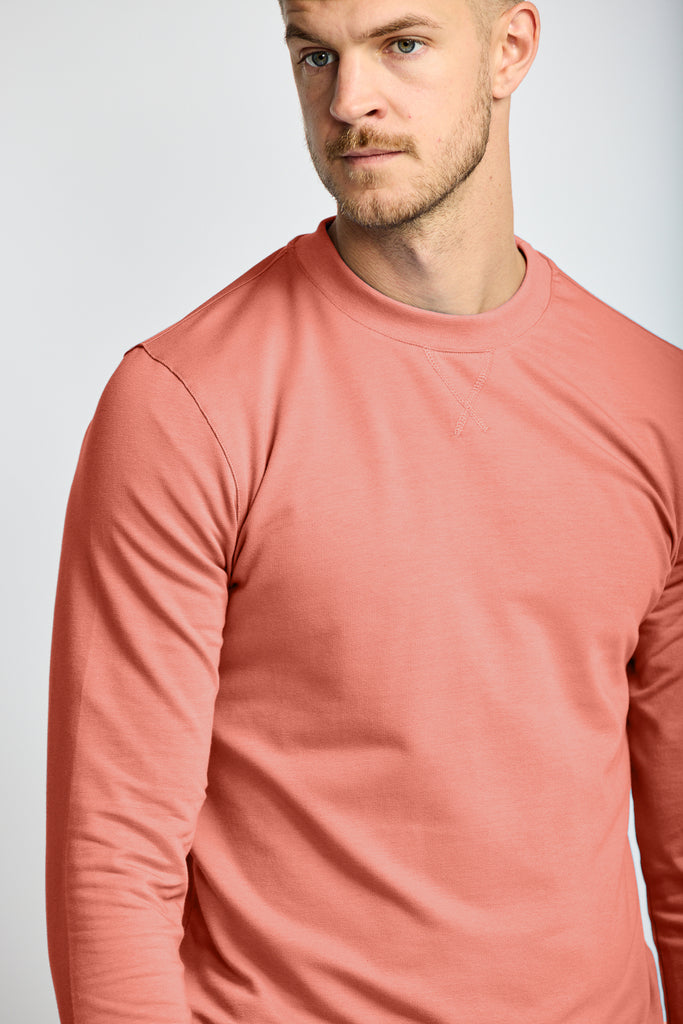 close up of front of model wearing Easy Mondays brand crew neck sweatshirt in light pink salmon color