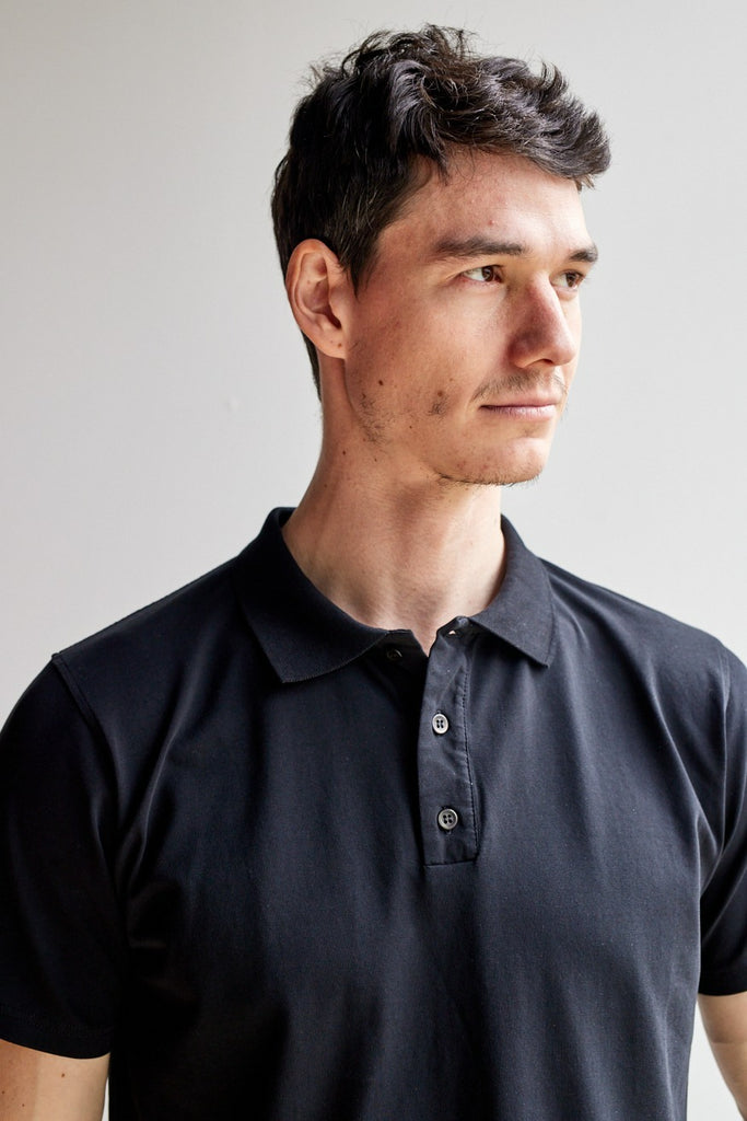 close up of model wearing Easy Mondays black short sleeved polo shirt with color-matched buttons