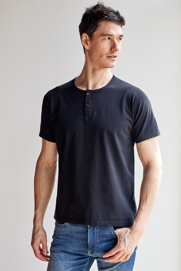 front view of model wearing Easy Mondays black short sleeved Henley shirt with color-matched buttons