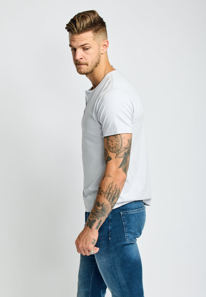 side view of model wearing Easy Mondays short sleeved Henley shirt in off white cloud color with color matched buttons