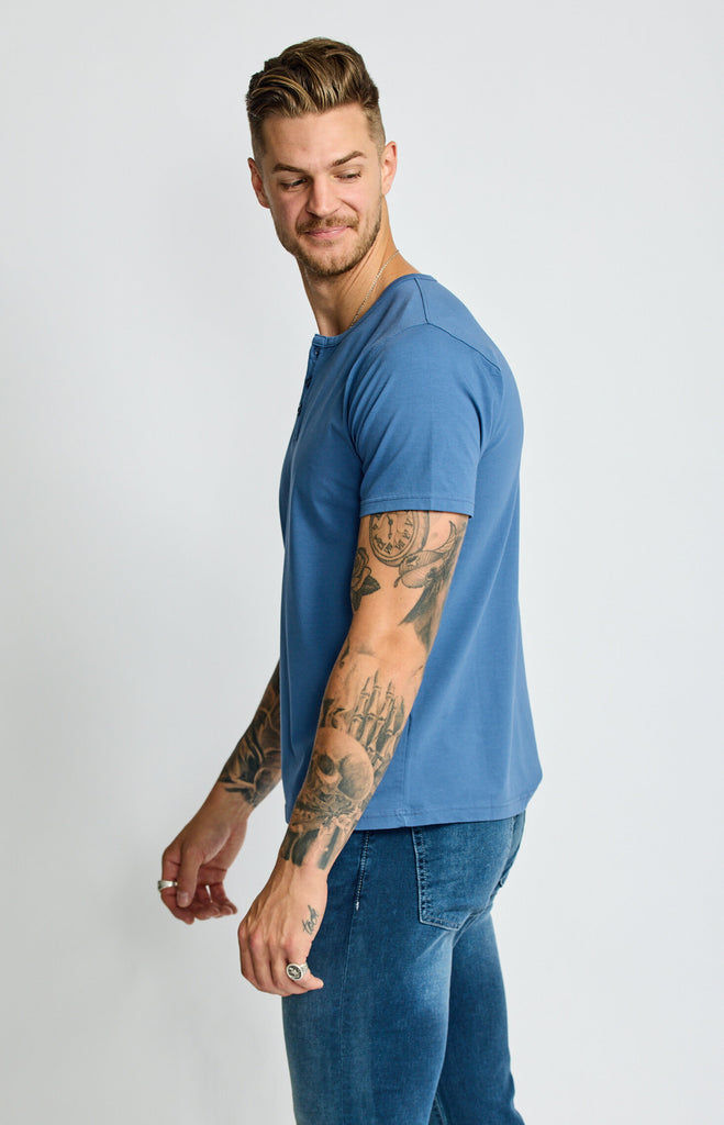 side view of model wearing Easy Mondays short sleeved Henley shirt in light ocean blue with color matched buttons