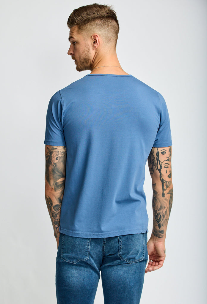 back of model wearing Easy Mondays short sleeved Henley shirt in light ocean blue with color matched buttons