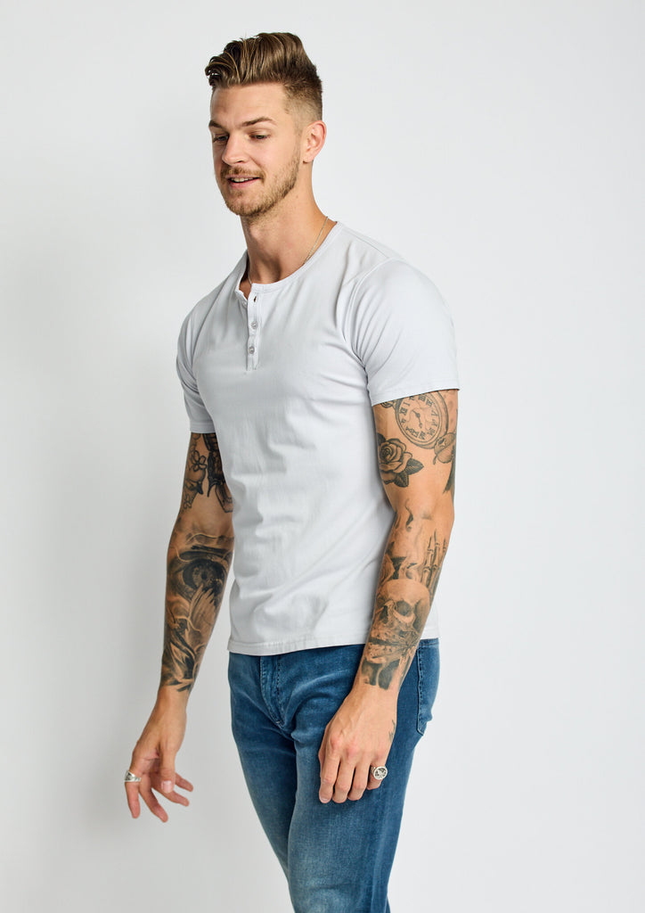 angled side view of model wearing Easy Mondays short sleeved Henley shirt in off white cloud color with color matched buttons